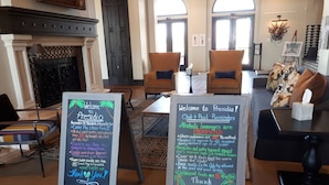 Een lobby met twee prikborden waarop herinneringen en regels voor gasten staan, een open haard, een zithoek en een uitzicht door grote ramen.