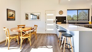 A modern kitchen with a white island, wooden chairs, and a large window.