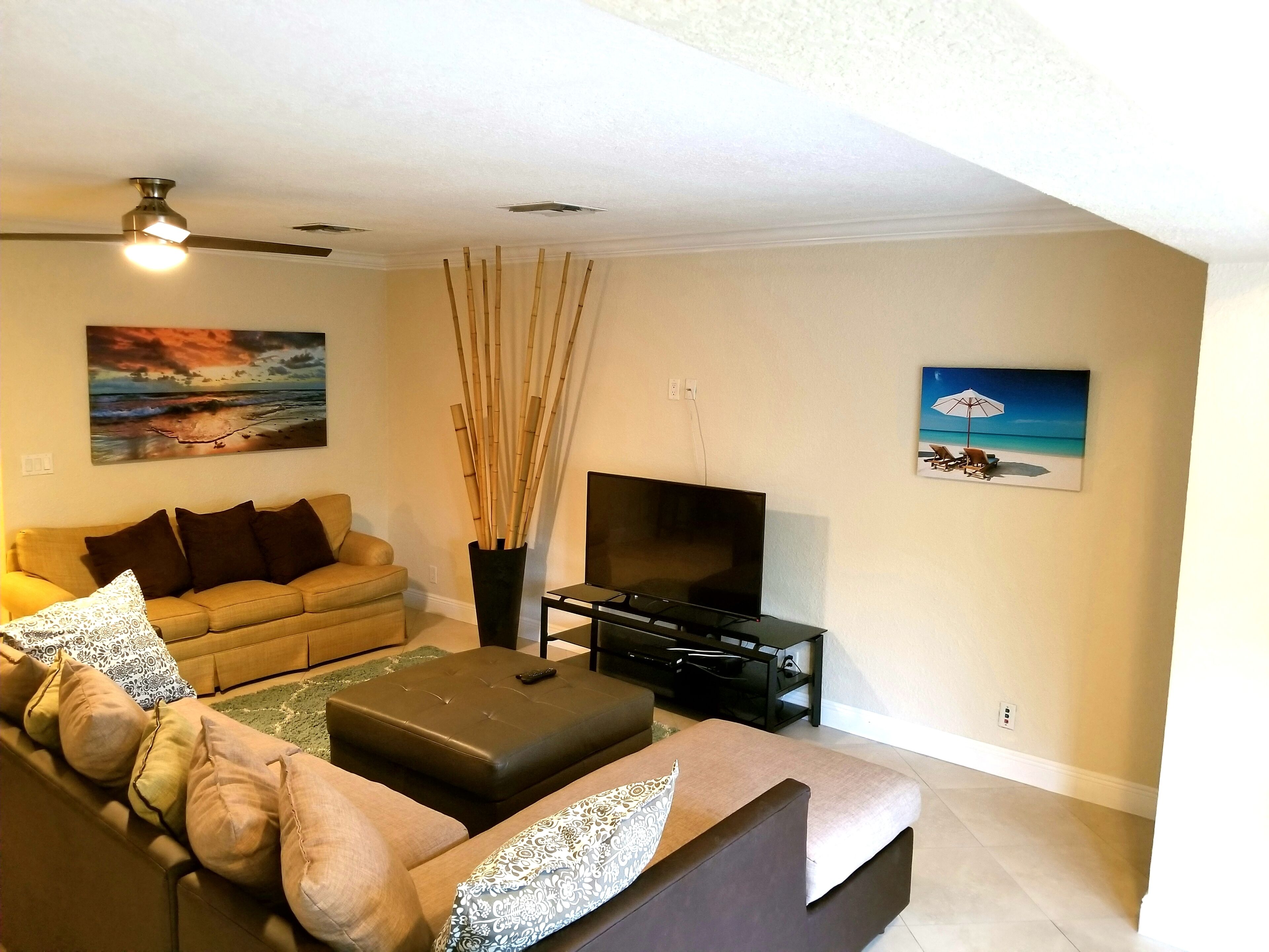 A living room with a sofa, ottoman, TV stand, and decorative elements like a painting and bamboo sticks.