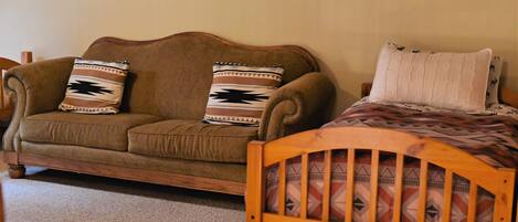 A brown sofa with patterned pillows and a wooden bed with a patterned bedspread.