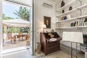Una habitación con zona de comedor, un mueble de madera con una guitarra, un atril con partituras y una estantería con libros y objetos decorativos.