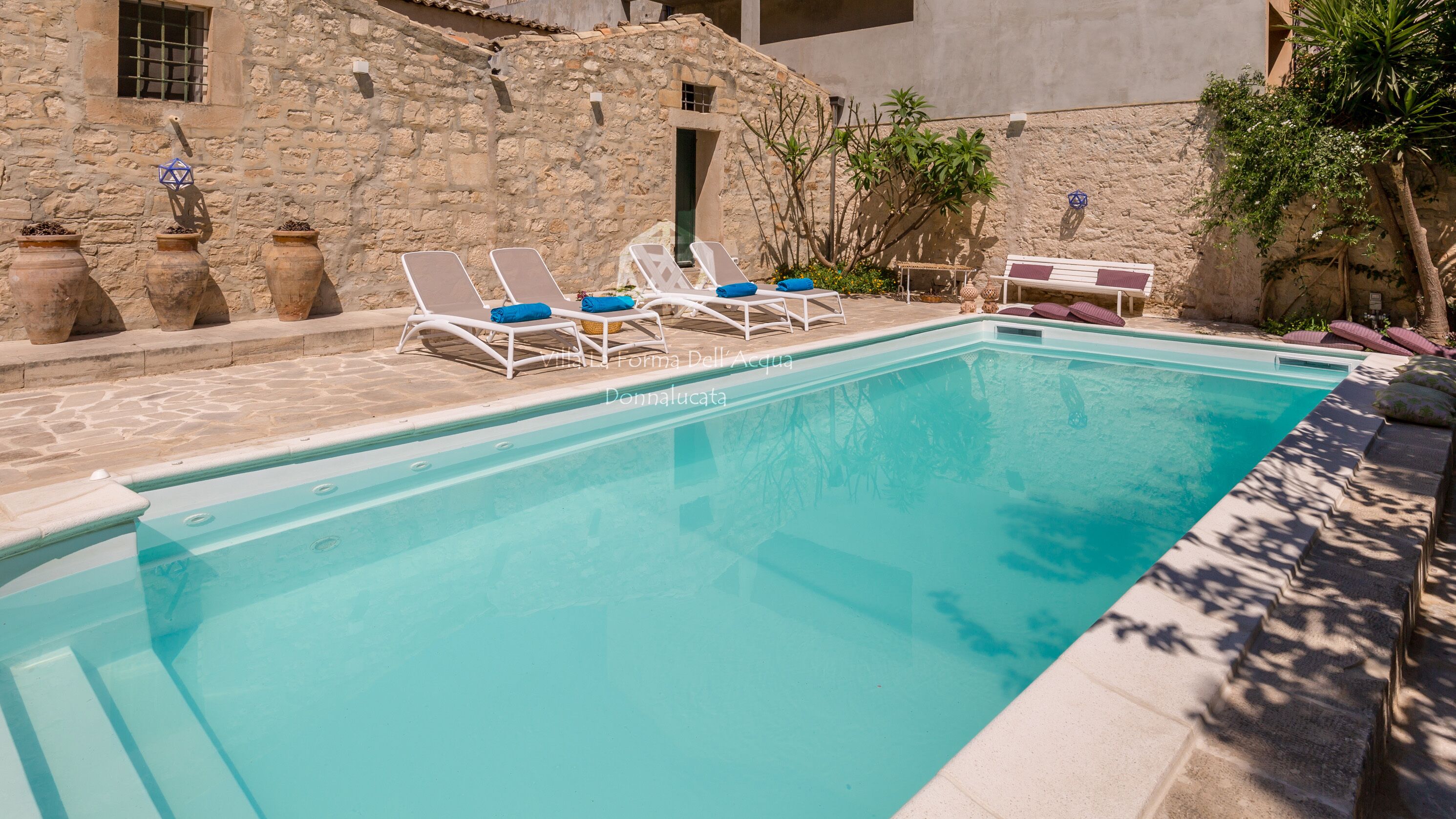 Une piscine avec des chaises longues et un mur de pierre en arrière-plan.