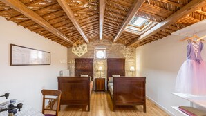 Una stanza con pavimento in legno, parete in pietra e tetto di paglia. Sono presenti due letti con testiere in legno e un tavolo con una sedia.