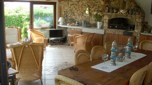 Un coin repas chaleureux, avec des meubles en osier, une cheminée en pierre et un téléviseur.