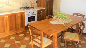 A kitchen with wooden cabinets, a stove, and a dining table with chairs. - Guidaloca Bay House Scopello with mini-pool (Castellammare del Golfo)