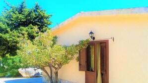 A building with a stone base and a yellow wall, a wooden door with shutters, and a small lamp above it. - Guidaloca Bay House Scopello with mini-pool (Castellammare del Golfo)