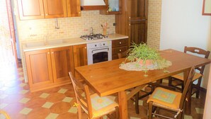 A kitchen with wooden cabinets, a stove, and a dining table with chairs. - Guidaloca Bay House Scopello with mini-pool (Castellammare del Golfo)
