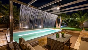 Una piscina con cascada, mobiliario exterior y un área de patio techada.
