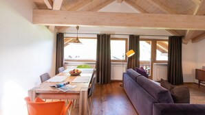 A dining area with a wooden table, chairs, and a sofa. There are windows with curtains and a radiator. - 100sqm apartment in central location in Lutago with three rooms (Lutago)