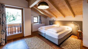 A bedroom with a wooden ceiling, a large window with curtains, a bed with white linens, and a small bedside table with a lamp. - 100sqm apartment in central location in Lutago with three rooms (Lutago)