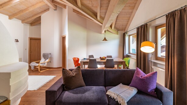 A cozy living room with a dark-colored sofa, a wooden ceiling, and a dining area in the background. - 100sqm apartment in central location in Lutago with three rooms (Lutago)