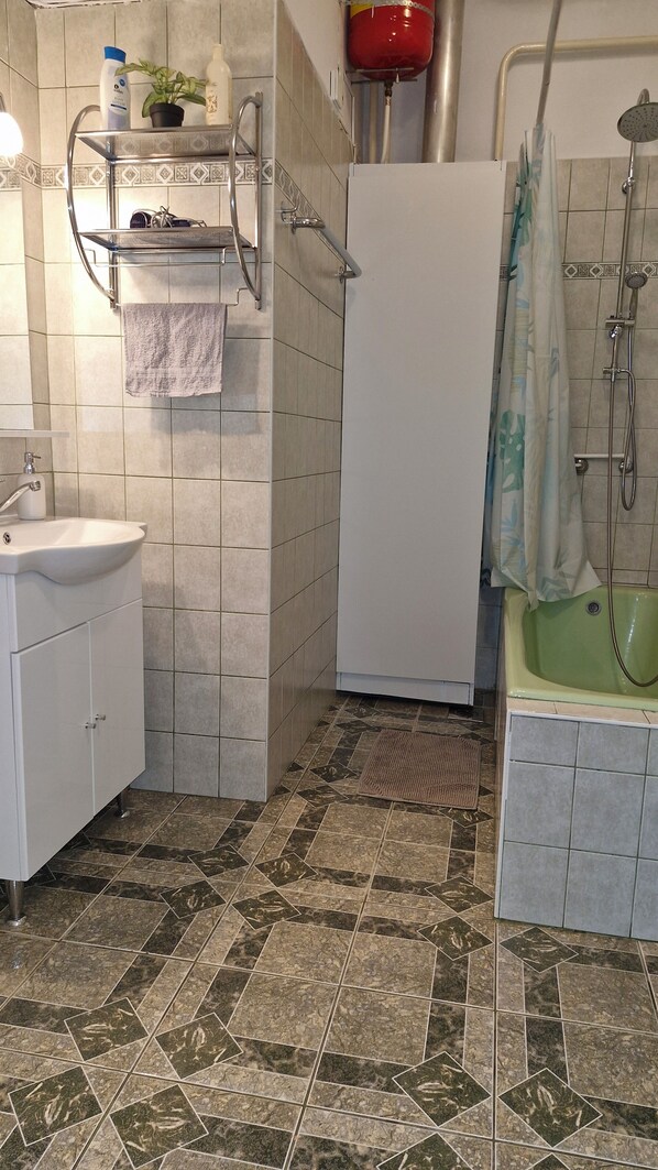 A bathroom with a sink, mirror, towel rack, shower, and a green bathtub.