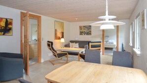 A modern living room with a wooden dining table, two armchairs, a sofa, and a ceiling light.