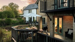 A deck with a table set for dining, a barbecue grill, and a balcony with outdoor furniture.