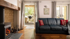 A cozy living room with a fireplace, a dark leather sofa with red cushions, and a view of the outdoors.