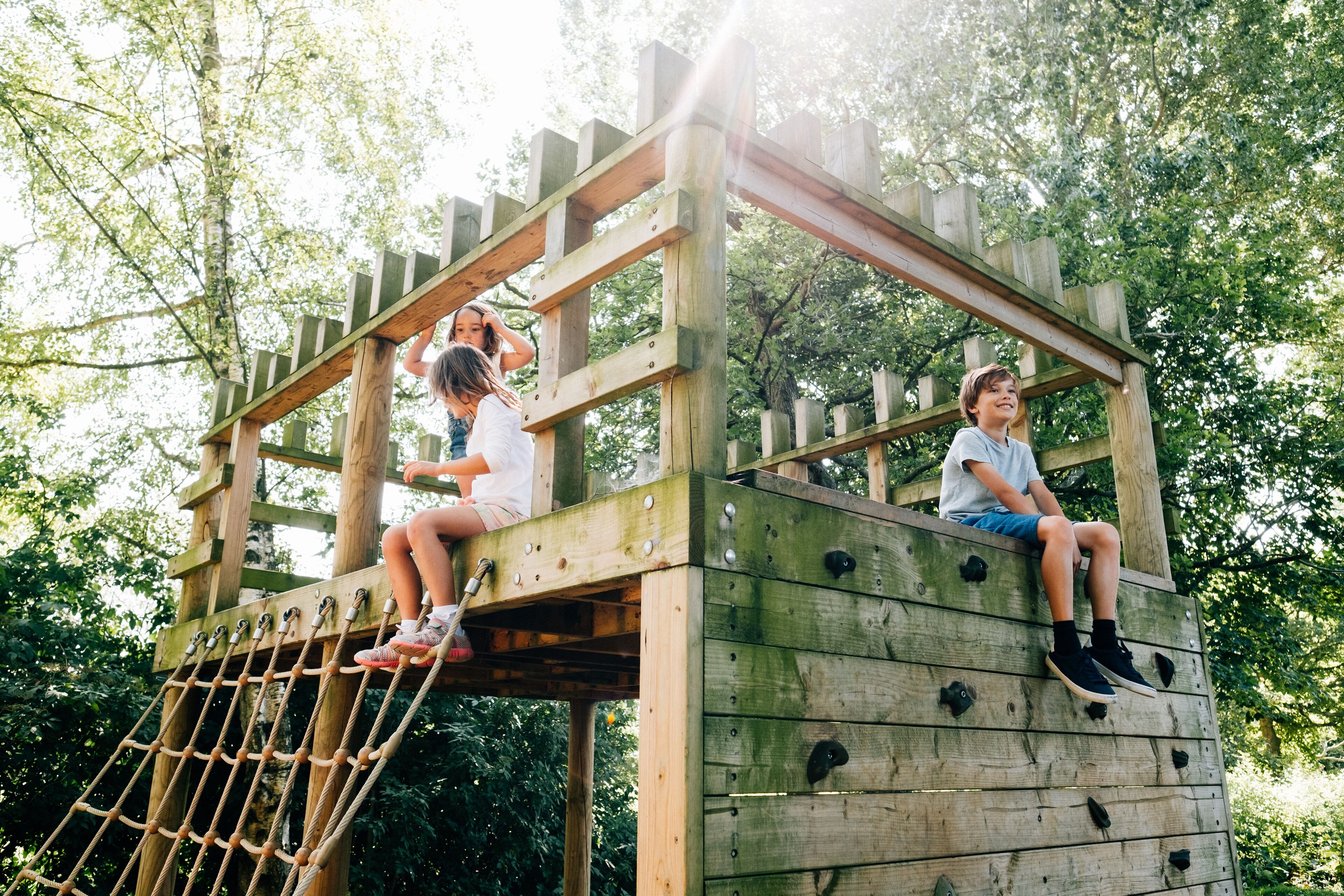Deux enfants grimpent sur une structure d’escalade en bois, à l’aide d’une échelle de corde.