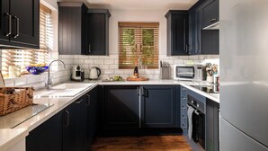 A modern kitchen with dark cabinetry, a stainless steel refrigerator, a microwave, and a coffee maker.