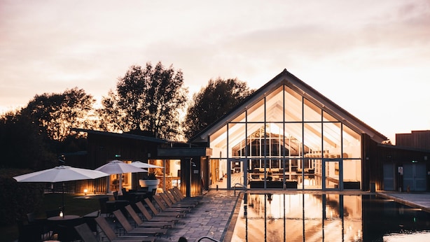 A modern building with a glass facade, outdoor seating with umbrellas, and a pool area.
