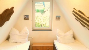 A small, triangular room with two beds, a window, and a radiator.
