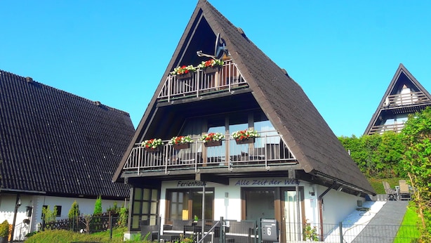 A traditional chalet with a steeply pitched roof, a balcony with flower boxes, and a sign reading "Ferienhaus".