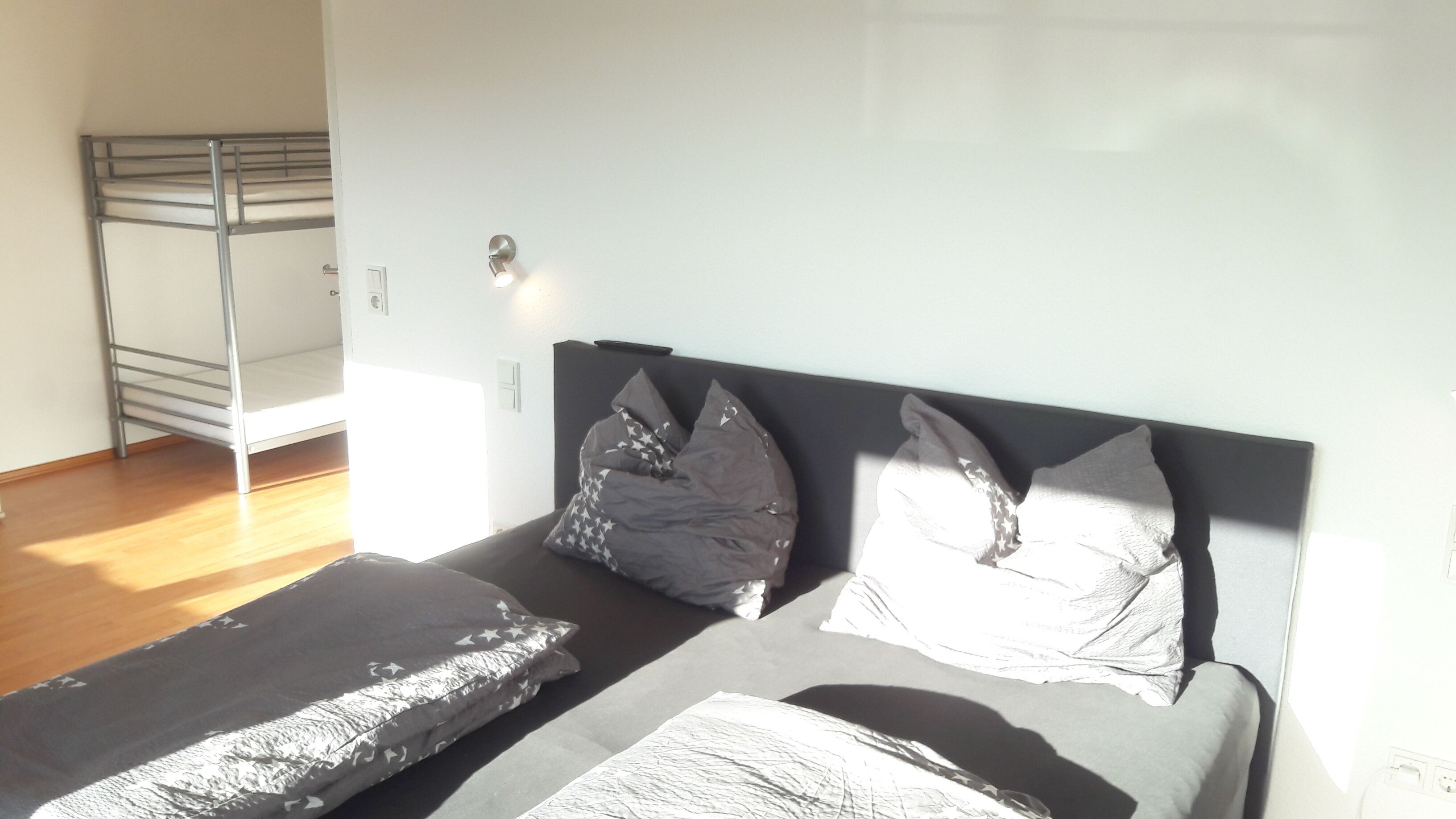 A bedroom with a bunk bed, two pillows with star patterns, a bedside table, and a wall socket.