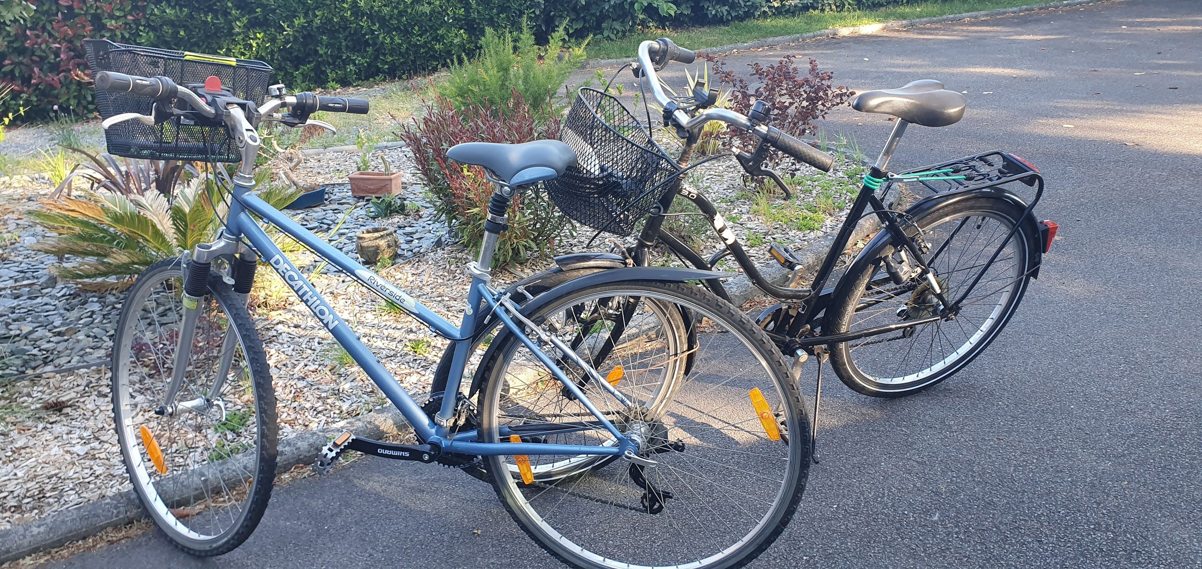 Deux vélos sont garés sur une surface pavée, avec un jardin et une zone recouverte de gravier en arrière-plan.