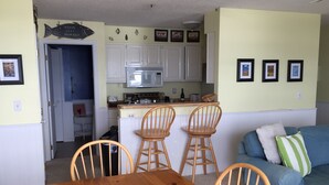 A dining area with a wooden table and four wooden chairs, a kitchen with white cabinets and a microwave, and a blue sofa with a striped pillow. - Escape To Madeline Island !  Superior Lakefront 2 Bedroom Condo  (La Pointe)
