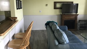 A living room with a grey sofa, wooden chairs, a TV, and a fireplace. - Escape To Madeline Island !  Superior Lakefront 2 Bedroom Condo  (La Pointe)