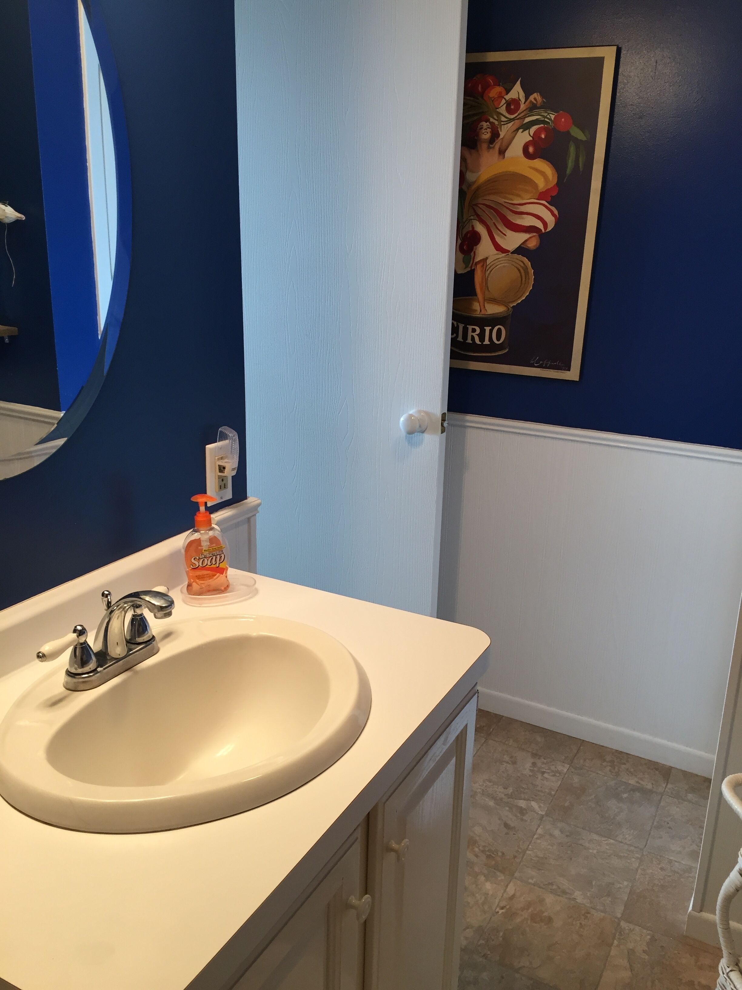 A bathroom with a white sink, a mirror, a soap dispenser, and a framed picture on the wall.