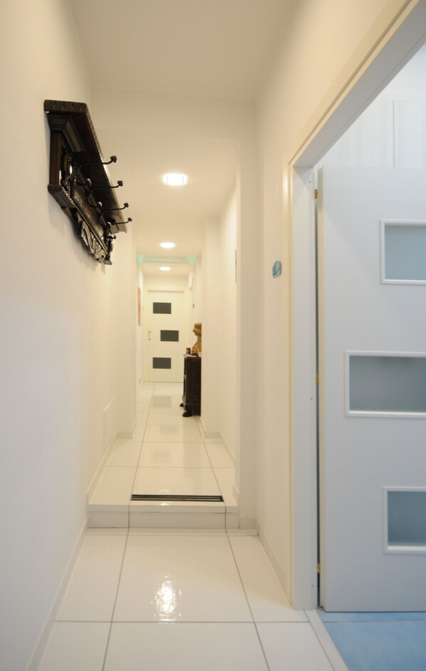 A hallway with a white tiled floor, a coat rack on the left, and a door with a window on the right.