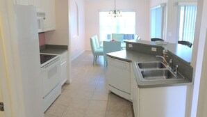 A kitchen with white cabinets, a stove, and a sink. There is a dining area with a chair and a table. - Charmer in the Heart of Cape Coral (Cape Coral)