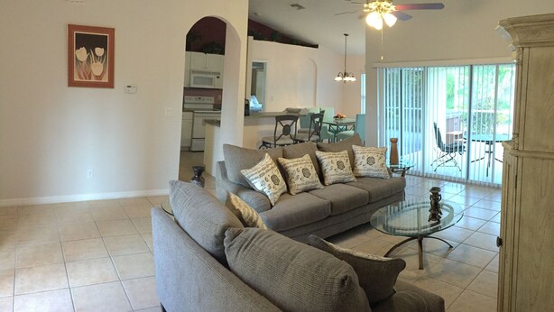 A spacious living room with a grey sectional sofa, a glass coffee table, and a dining area in the background. - Charmer in the Heart of Cape Coral (Cape Coral)
