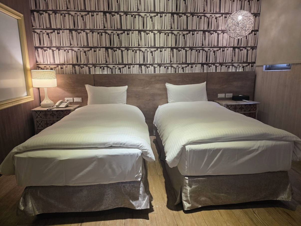 Une chambre d’hôtel avec deux lits, un mur entier recouvert d’étagères, une lampe de chevet et un téléphone sur la table de chevet.
