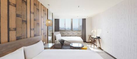 A hotel room with a large bed, a desk with a chair, a view of the city through a large window, and a wooden accent wall.
