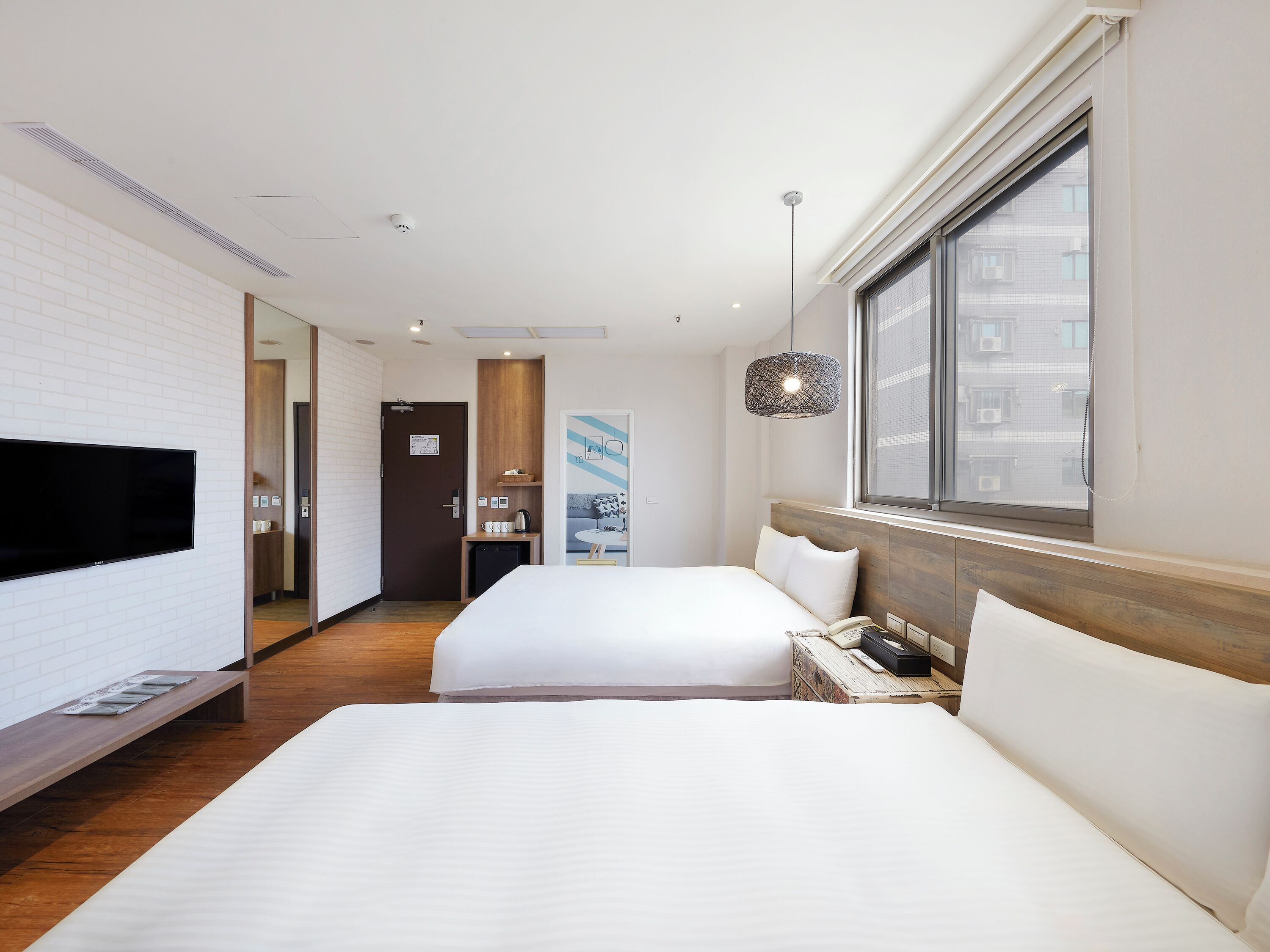 A hotel room with two beds, a TV, a desk, a window, and a door.