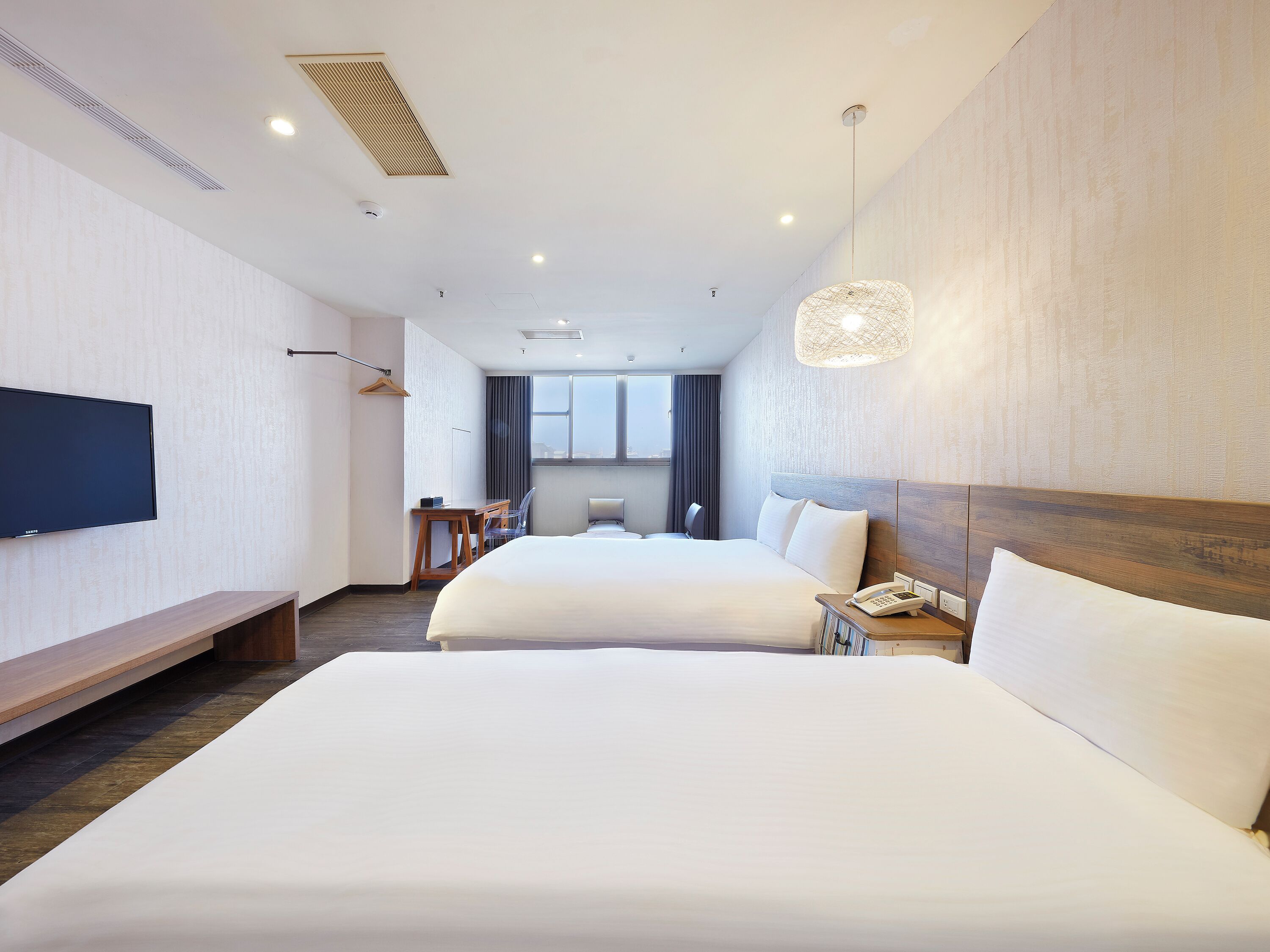A hotel room with two beds, a flat-screen TV, a desk, and a large window.
