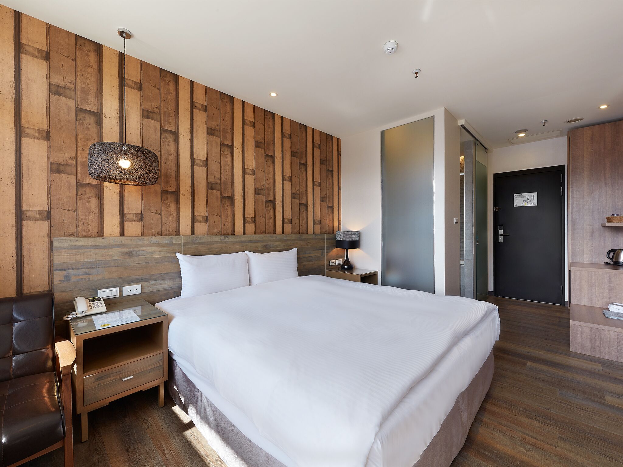 A hotel room with a large bed, wooden panel wall, a desk with a lamp, a phone, and a chair.