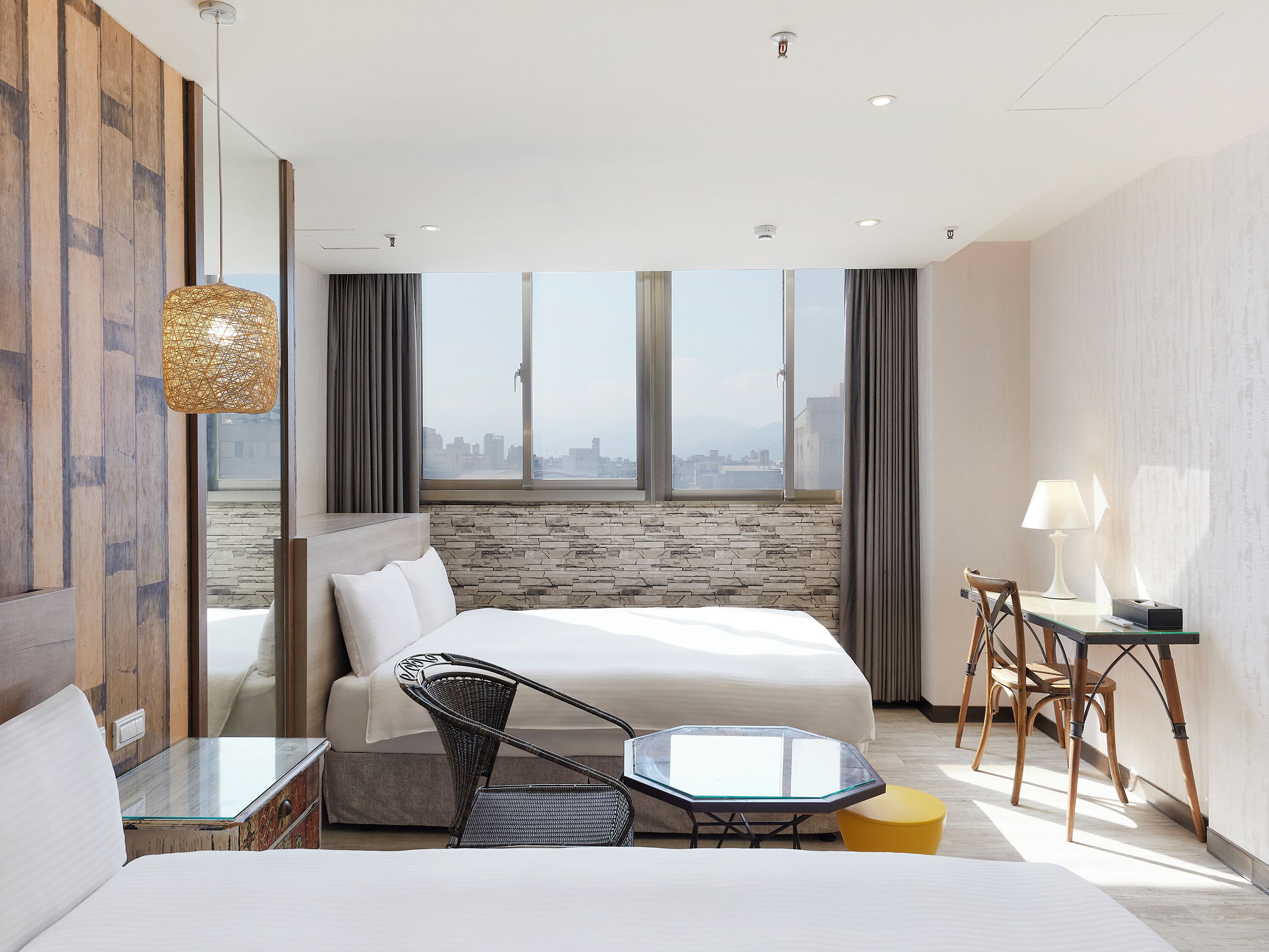 Une chambre d’hôtel moderne avec un grand lit, une table en verre, une chaise, un bureau et une vue sur la ville.