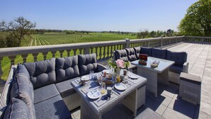 A terrace with outdoor furniture, a dining table set, and a view of a vineyard.