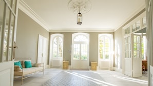 A spacious room with a large window, a sofa, a patterned rug, and a ceiling fan.