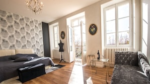 A spacious bedroom with a large bed, a sitting area with a sofa, a chandelier, and a view through the open door.