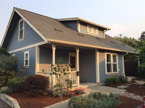 A two-story house with a gabled roof, a front porch with a railing, and a small garden with various plants and flowers.
