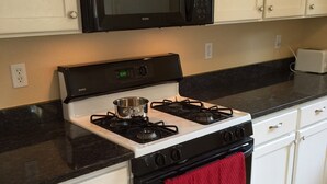A kitchen with white cabinets, a black microwave, a stove with a red towel, and a toaster. - BLOSSOM VIEW COTTAGES: Luxurious 3 Bedroom + Den  Near Theaters, Downtown (Ashland)