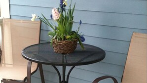A round metal table with a woven basket containing flowers, two brown chairs, and a blue exterior wall. - BLOSSOM VIEW COTTAGES: Luxurious 3 Bedroom + Den  Near Theaters, Downtown (Ashland)