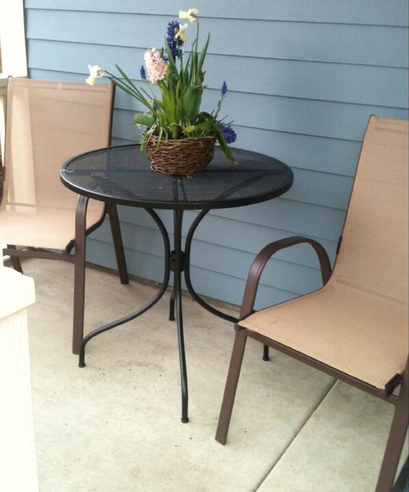 A round metal table with a woven basket containing flowers, two brown chairs, and a blue exterior wall.