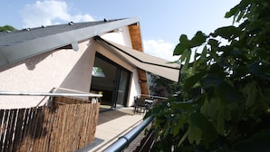 Um edifício moderno com telhado inclinado, cerca de madeira e varanda com mobiliário para área externa.