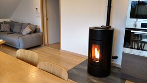 Uma sala de estar moderna com uma lareira a lenha, um sofá cinzento e um espaço de refeições com mesa e cadeiras de madeira.