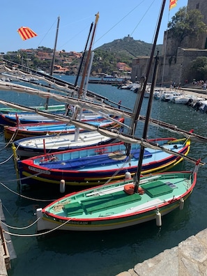 Un puerto deportivo con barcos de colores amarrados, un muro de piedra al fondo y un cielo despejado.