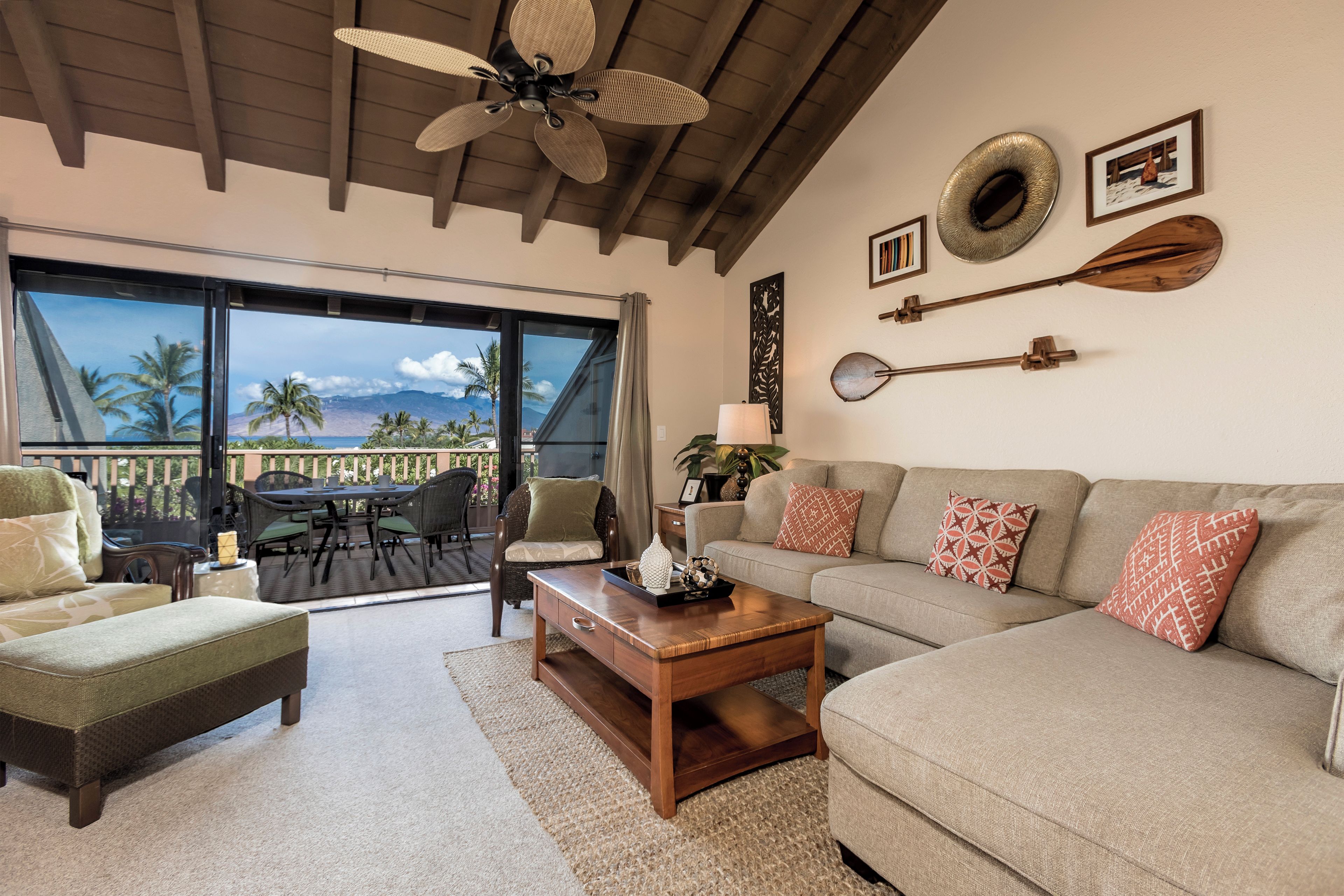 A spacious living room with a large window, a ceiling fan, and a view of palm trees.