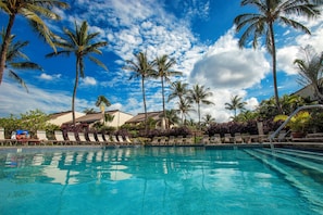 A pool area with clear blue water, surrounded by palm trees and lounge chairs.